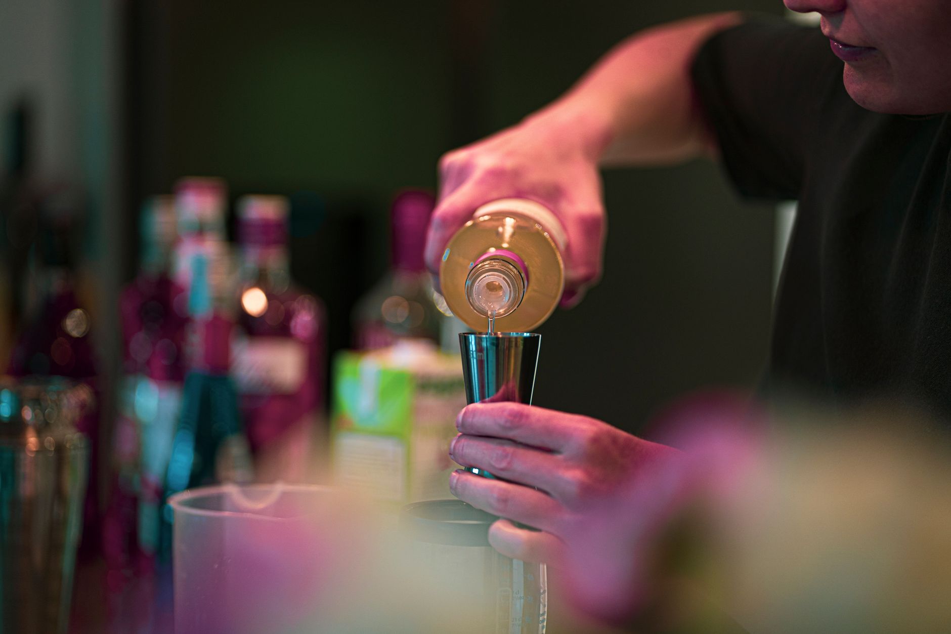 Bartender pouring a drink into a jigger at a bar, similar to what the Barsys 360 automates