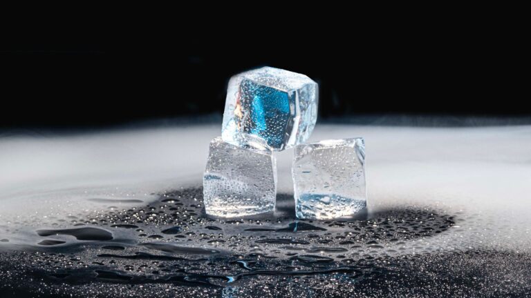 Ice cubes melting into water on a dark counter, the core problem a countertop ice maker with an insulated bin solves