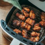 Crispy chicken pieces cooking in a modern basket air fryer on a kitchen counter