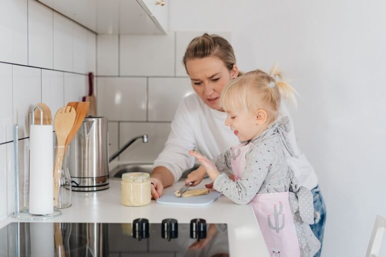 Toddler standing on a learning tower helping at a kitchen counter, illustrating the Boon PIVOT toddler tower recall and safer alternatives