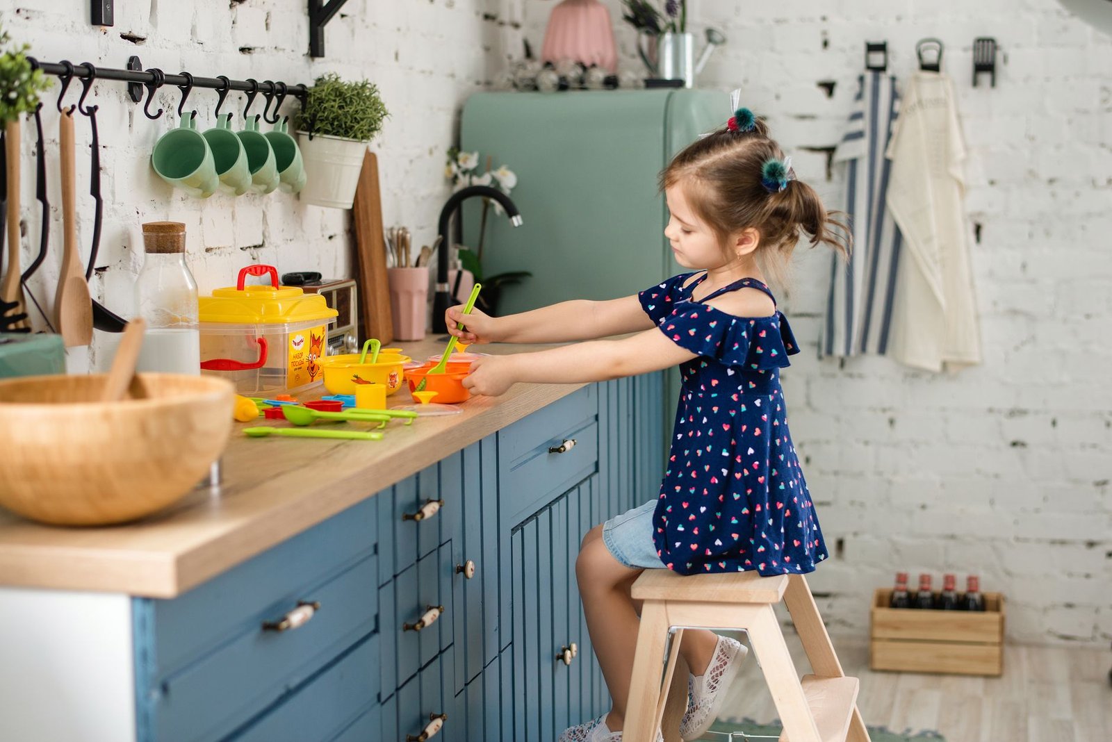 Child cooking at a kitchen counter on a step stool, an alternative to the recalled Boon PIVOT collapsible toddler tower