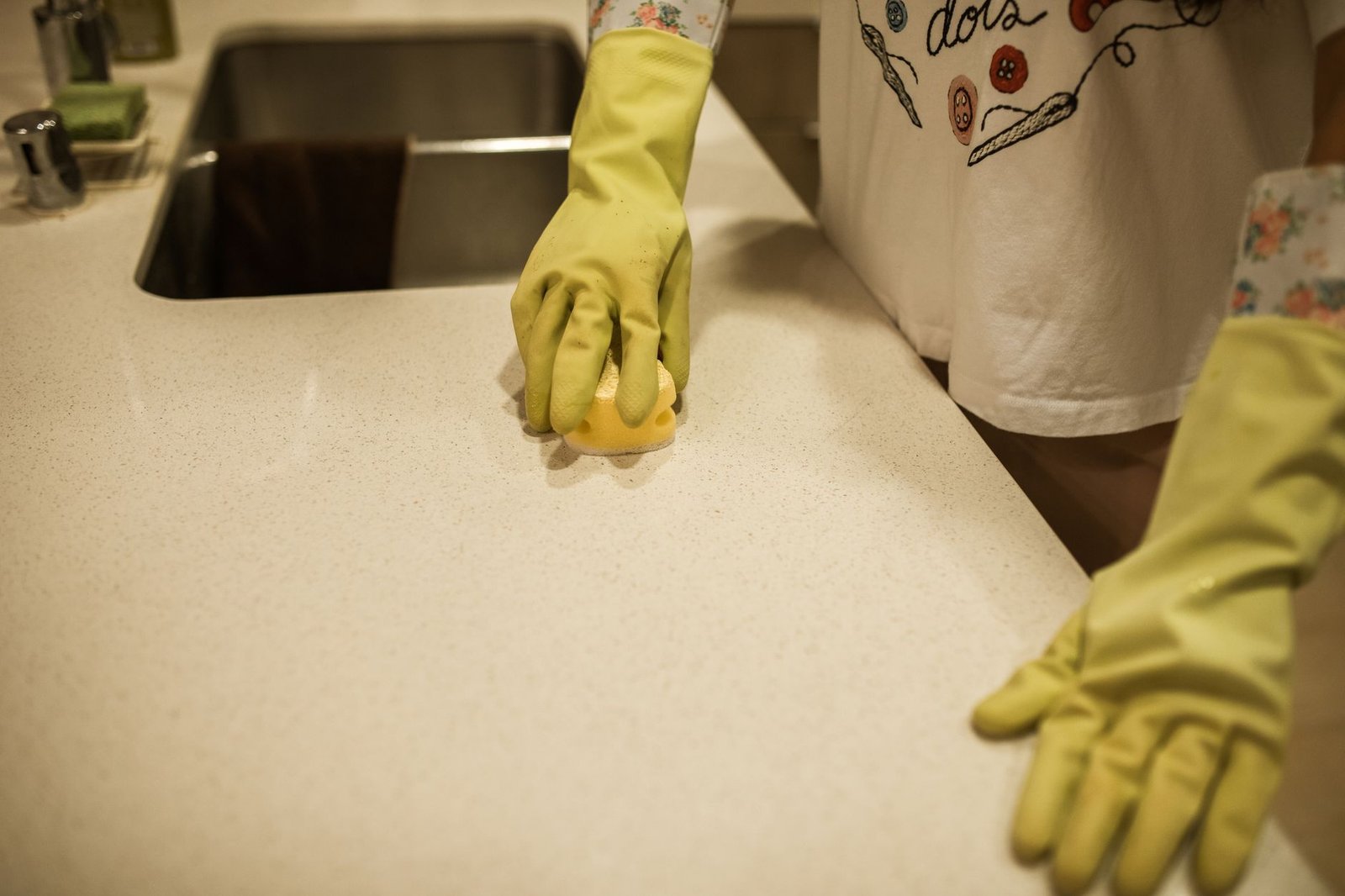 Person in yellow rubber gloves cleaning a kitchen surface, the same routine used to clean a countertop ice maker