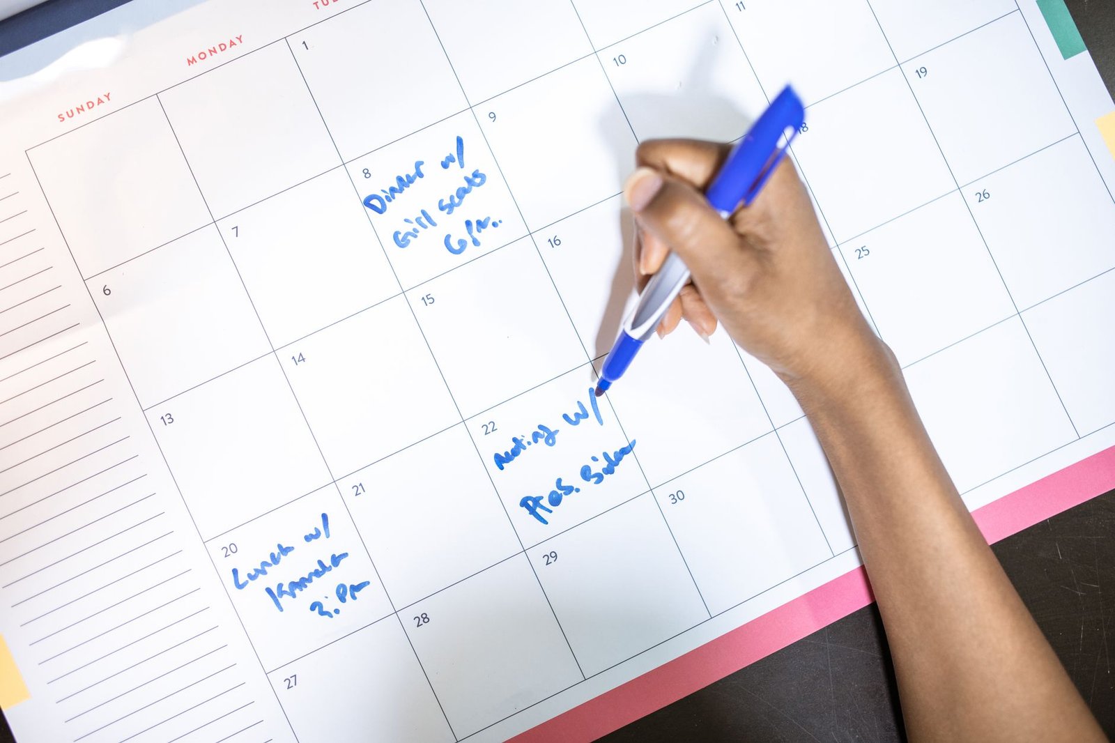 A person writing appointments on a calendar, the analog habit a Cozyla digital calendar replaces